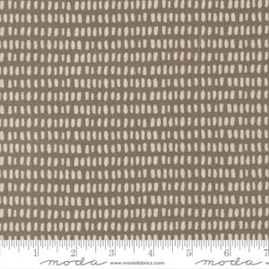May include: A close-up of fabric with a repeating pattern of white dashes on a muted olive-green background. The fabric is marked with a ruler along the bottom edge, showing inch measurements.