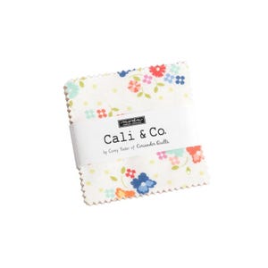 May include: A white fabric square with a floral print in shades of pink, blue, yellow, and green. The fabric has a label that reads "Cali & Co. by Corey Yoder of Coriander Quilts."