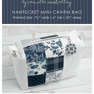May include: A white quilted mini-charm bag with a patchwork design featuring blue floral and plaid patterns. The bag has a zipper closure, a decorative charm, and white handles. The finished size is 7.5 inches wide, 6 inches tall, and 2.75 inches deep.