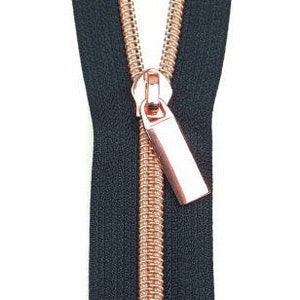 May include: A black zipper with a rose gold slider and pull tab. The zipper is open and the slider is in the middle of the zipper.