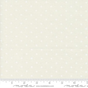 May include: Cream-colored fabric with a repeating pattern of white polka dots. The fabric has a textured appearance and a ruler is visible along the bottom edge, marked in inches. The fabric is from Moda Fabrics.