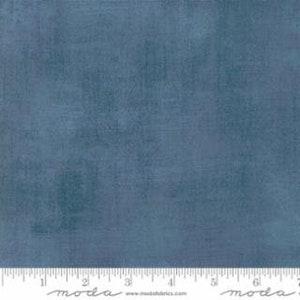 May include: A solid blue fabric with a textured appearance. The fabric is marked with a ruler showing measurements in inches. The fabric is likely used for quilting or sewing projects.