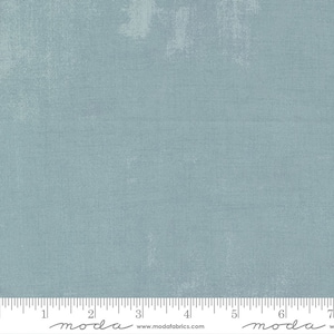 May include: A solid blue fabric with a subtle textured pattern. The fabric is a light blue color with a slightly faded look. The fabric is shown with a ruler for scale.