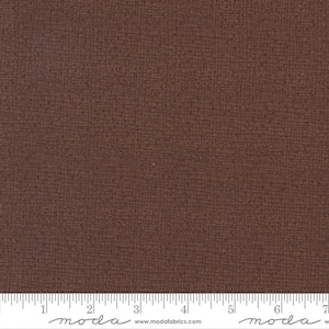 May include: A close-up of a brown fabric with a subtle textured pattern. The fabric is measured with a ruler in inches.