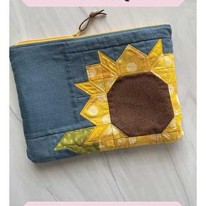 May include: A blue and yellow fabric pouch with a sunflower design. The pouch is 8 inches by 10 inches and has a zipper closure. The text "Sunflower Pouch" is printed on the top of the image. The text "Finished Size 8" x 10" is printed below the pouch. The text "Sew Lux Fabric" is printed below the pouch.
