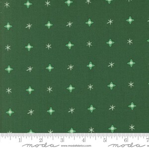 May include: Dark green fabric with a repeating pattern of white snowflakes and four-leaf clovers in light green. The fabric has a ruler along the bottom edge with the word "moda" and the website "www.modafabrics.com".