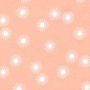 May include: A repeating pattern of white starburst shapes scattered across a peach-colored background. The starbursts have multiple rays emanating from a central point, creating a textured, floral-like design. The pattern is evenly distributed.