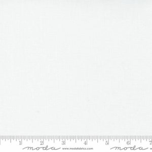 May include: A plain white fabric with a subtle texture. The fabric is measured with a ruler in inches. The ruler has the word "moda" printed on it.