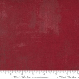 May include: A solid red fabric with a subtle textured pattern. The fabric is a deep red color with a slight sheen. The fabric is shown with a ruler for scale.