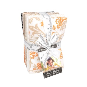 May include: A stack of fabric squares tied with a white ribbon printed with measurements. The fabric features a floral pattern in orange and beige on a white background. A tag with the "moda fabrics + supplies" logo is attached.