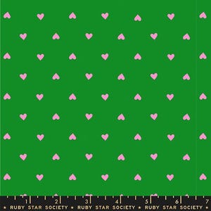 May include: Green fabric with a repeating pattern of small, pink hearts. The hearts are evenly spaced across the surface. The bottom of the fabric has a ruler and the text "RUBY STAR SOCIETY".