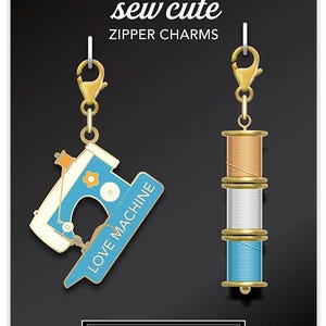 May include: Two zipper charms with gold-colored clasps. One charm is a blue and white sewing machine with the text "LOVE MACHINE". The other charm is three spools of thread in orange, white, and blue. The text "CATHE HOLDEN'S sew cute ZIPPER CHARMS" is at the top.