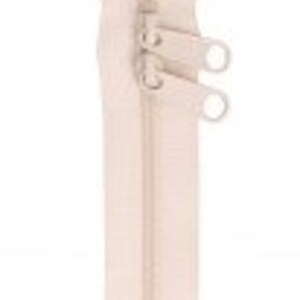 May include: A beige zipper with two pull tabs. The zipper is closed and has a smooth finish.