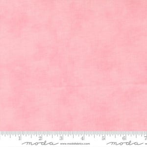 May include: A solid pink fabric with a subtle, mottled texture. The fabric has a soft, watercolor-like appearance. A ruler is at the bottom of the image, with the brand name "moda" visible.