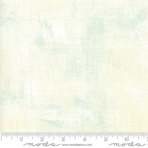 May include: A white fabric with a subtle green and yellow distressed pattern. The fabric has a soft, textured feel and is perfect for quilting, crafts, and home decor projects. The fabric is marked with a ruler and the word "moda" in a handwritten font.