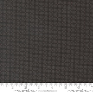 May include: Dark gray fabric with a repeating geometric pattern. The fabric has a subtle texture and a ruler is visible along the bottom edge, marked in inches. The fabric is suitable for quilting, sewing, or other craft projects.