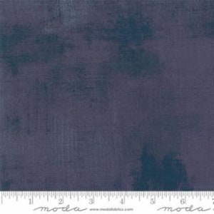 May include: A close-up of a fabric with a mottled, distressed appearance. The fabric is primarily a deep indigo blue with darker blue and gray accents. A ruler is placed along the bottom edge, showing measurements in inches.