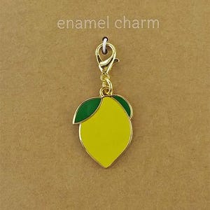 May include: A yellow lemon-shaped enamel charm with a green leaf, attached to a gold-tone lobster clasp. The charm is mounted on a brown display card featuring the text enamel charm at the top and JEWELRY MADE BY ME at the bottom.