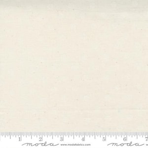May include: Cream-colored fabric with a subtle, textured pattern. The fabric has a grid-like design with small, repeating shapes. A ruler is placed along the bottom edge, marked in inches. The fabric is likely used for quilting or other craft projects.
