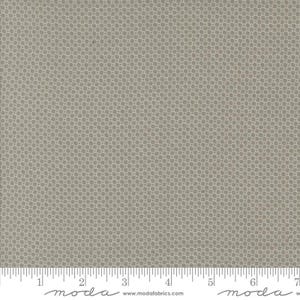 May include: Close-up of a fabric with a repeating pattern of small, light gray squares on a darker gray background. The fabric has a subtle texture and is measured with an inch ruler at the bottom. The fabric is from Moda Fabrics.