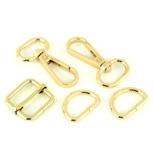 May include: A collection of gold-colored metal hardware components, including two swivel clasps, a rectangular slider buckle, and two D-rings. These pieces are likely for bag making or other craft projects.