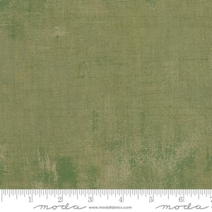 May include: Green fabric with a textured, distressed appearance. The fabric has a mottled effect with lighter areas, creating a vintage or rustic aesthetic. The fabric is marked with a ruler along the bottom edge.