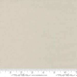May include: A solid, light beige fabric swatch with a subtle texture. The fabric is measured in inches with the text "moda" printed on the ruler.