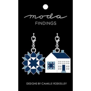 May include: A pair of earrings featuring a blue and white starburst design and a blue and white house design. The earrings are silver and have a hook closure. The earrings are labeled "moda FINDINGS" and "DESIGNS BY CAMILLE ROSKELLEY".