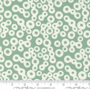 May include: A green fabric with a white pattern of circles and connected shapes. The fabric is from Moda Fabrics.