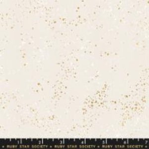 May include: Cream-colored fabric with a speckled gold pattern. The fabric has a subtle texture and a ruler is at the bottom. The fabric is likely cotton or a similar material, suitable for quilting or apparel.