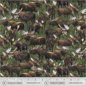 May include: Fabric with a repeating pattern of brown moose with large antlers on a green grassy background. The moose are in various poses, some standing and some walking. The fabric has a scale printed along the bottom with the words "WINDHAM FABRICS".