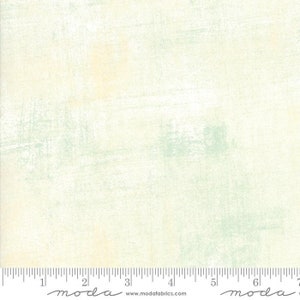 May include: A light green and cream fabric with a subtle distressed texture. The fabric has a soft, faded look, with hints of yellow and blue.