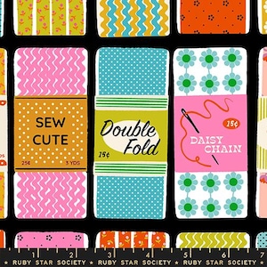 May include: A black fabric featuring a repeating pattern of vintage-style ribbon spools in various colors including pink, blue, orange, and green. The spools display text such as SEW CUTE, DOUBLE FOLD, and DAISY CHAIN, with a ruler at the bottom.
