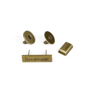 May include: Four antique gold-toned metal pieces: two round magnetic closures, a rectangular metal plate with the word "handmade" engraved on it, and a small rectangular metal plate.