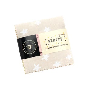 May include: A stack of beige fabric squares with white star patterns. The fabric is held together by a black band with the words "Ruby Star Society" and "Guaranteed Designs". A label reads "starry" and "new colors!" by Alexia Marcelle Abegg.
