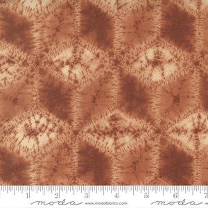 May include: Brown fabric with a repeating pattern of hexagonal shapes with a tie-dye effect. The fabric is textured and has a subtle sheen. The fabric is measured in inches.