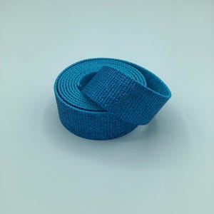 May include: A rolled-up, textured blue strap. The strap is a vibrant shade of blue, with a woven pattern visible on its surface. The material appears durable and flexible, suitable for various applications. The strap is coiled neatly, suggesting it's new or unused.