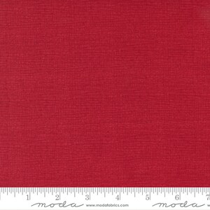 May include: A solid red fabric with a subtle textured pattern. The fabric is measured in inches with the text "moda" printed on the ruler.