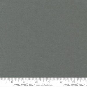 May include: A solid gray fabric with a subtle woven texture. The fabric is a muted, neutral shade, suitable for various sewing and crafting projects. A ruler is at the bottom of the image, with the word "moda" printed on it.