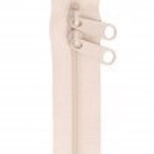 May include: A beige zipper with two pull tabs. The zipper is closed and has a smooth finish.