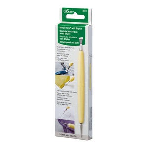 May include: A yellow Metal Hera with Stylus tool in its original packaging. The packaging is white and green with text in multiple languages. The tool has a metal tip and is designed for sewing and fabric work.