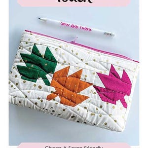 May include: A white quilted pouch with a pink zipper, featuring appliqued leaves in green, orange, and pink. The pouch is 6" x 10" and has the text "Autumn Breeze Pouch". A pen with "Sew Lux fabric" is also visible.