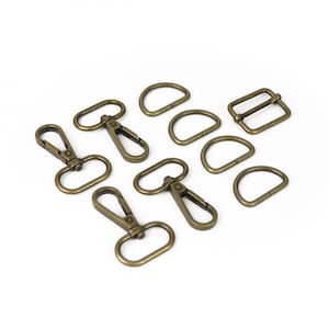 May include: A collection of antique brass-colored hardware components, including swivel clasps, D-rings, and a rectangular slider buckle. These metal findings are arranged on a white background, ideal for crafting and bag-making projects.