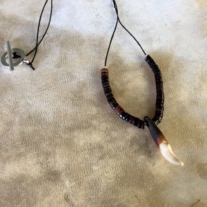 May include: A necklace with a brown and black beaded chain and a white tooth pendant.