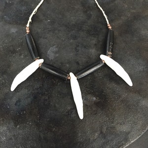 May include: A necklace made of black and white beads. The necklace has three white beads that resemble teeth and are attached to the black beads with a string.