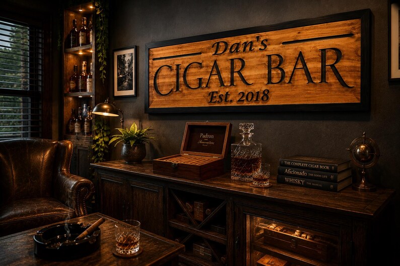 May include: A wooden sign that reads "Dan's CIGAR BAR Est. 2018" hangs above a wooden cabinet. A humidor, decanter, and books are on the cabinet. A leather chair and ashtray are in the foreground. The room has a dark, masculine aesthetic.