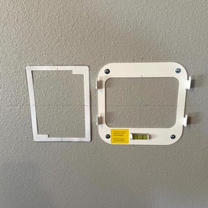 May include: Two white mounting brackets with screws and a level are displayed against a gray wall. One bracket is a paper template, and the other is a finished product. The finished bracket has a yellow sticker.