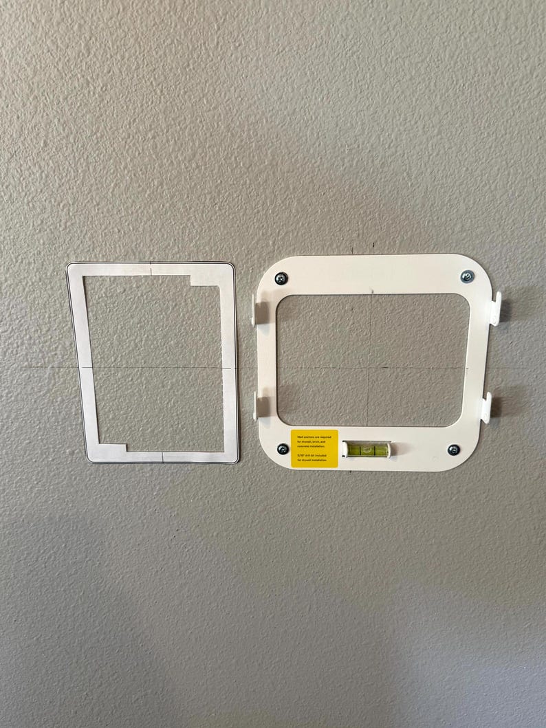 May include: Two white mounting brackets with screws and a level are displayed against a gray wall. One bracket is a paper template, and the other is a finished product. The finished bracket has a yellow sticker.