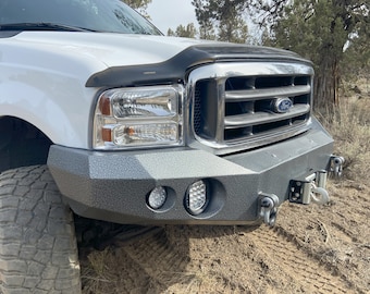May include: A white Ford pickup truck with a black front bumper and two round LED lights. The truck has a chrome grille and a Ford logo.