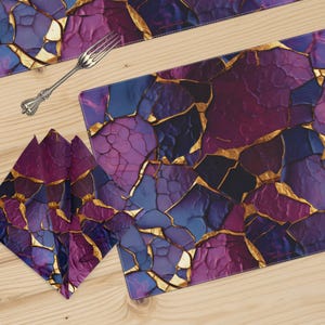 May include: A table setting featuring a placemat, napkins, and a runner with a purple, blue, and gold cracked stone design. A silver fork rests on the wooden surface. The napkins are folded and placed near the placemat.